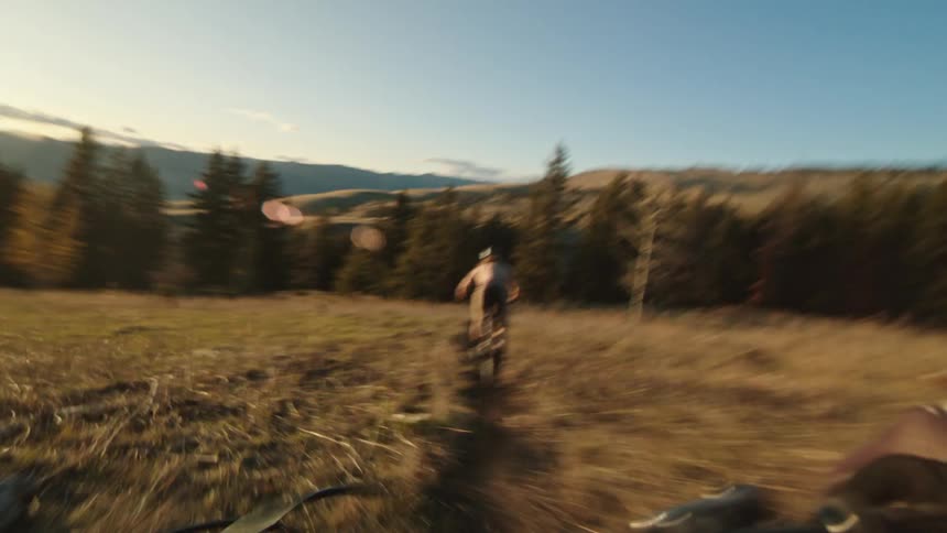 People are riding mountain bikes on a trail winding across grasslands in the evening