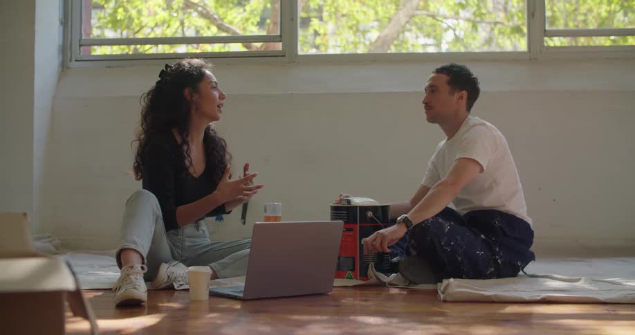 A man and woman are sitting on the floor by a laptop