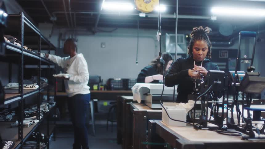 A woman checks inventory on the shelves as two others use heat presses to create graphic tees