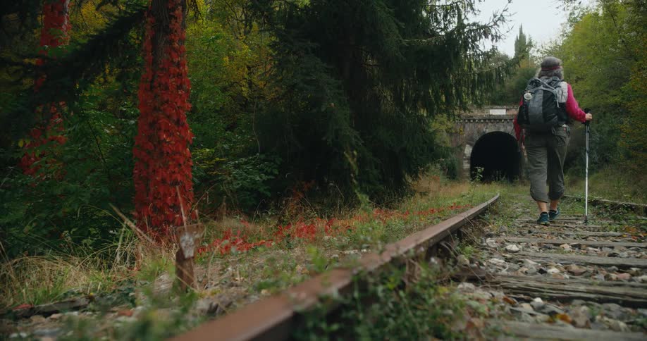 A hiker walks along an old railway towards an old stone tunnel