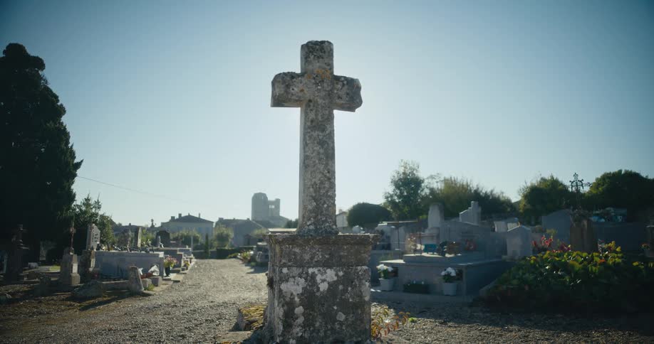A cross shaped tombstone in a cemetery under the daytime sky