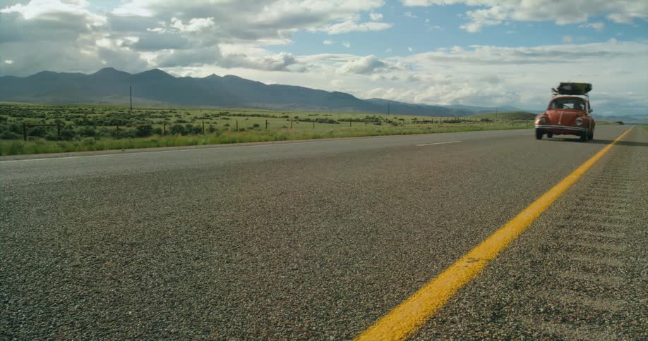 A car travels along a road through the countryside on a sunny day