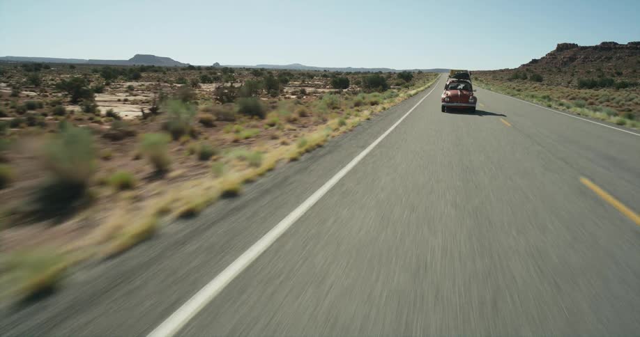 Red volkswagen bug drives along highway through scrub lands