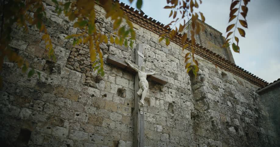 A sculpture of jesus on a wooden cross attached to a stone wall outdoors during the day