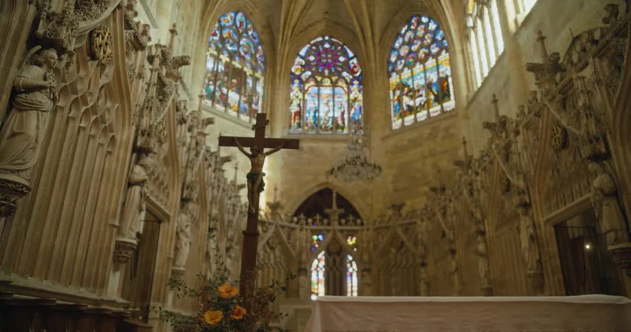 Sun shines through stained glass windows sitting near the ceiling in a ornately decorated cathedral
