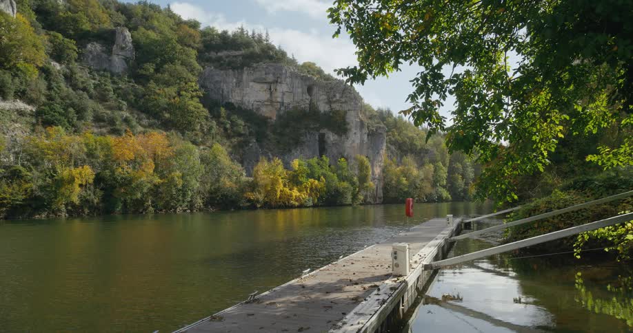 An empty dock in a river with rocky cliffs and trees on a beautiful scenic day