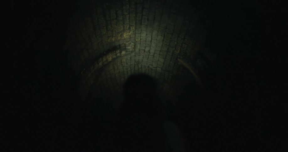 A man shines a flashlight in a dark tunnel