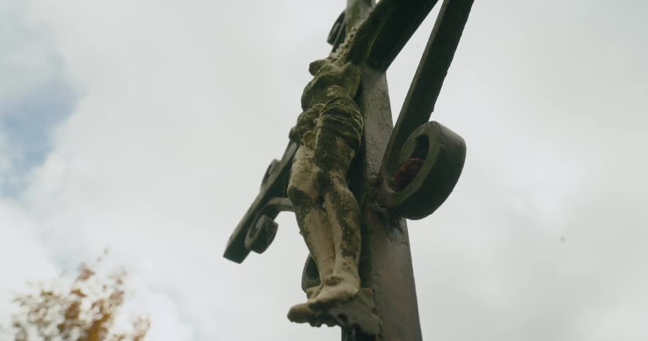 Statue of the crucifixion stands outdoors under a cloudy sky