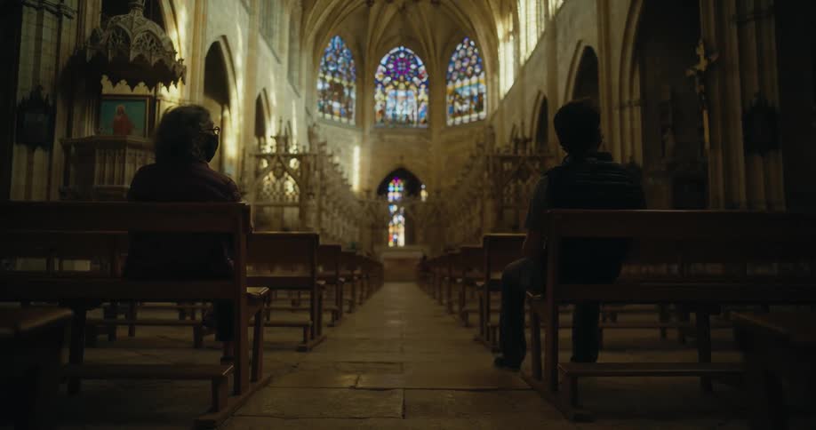 Two people are sitting on benches in the back of a cathedral