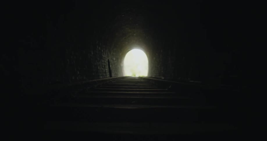Train tracks lead through brick walled tunnel to bright exit