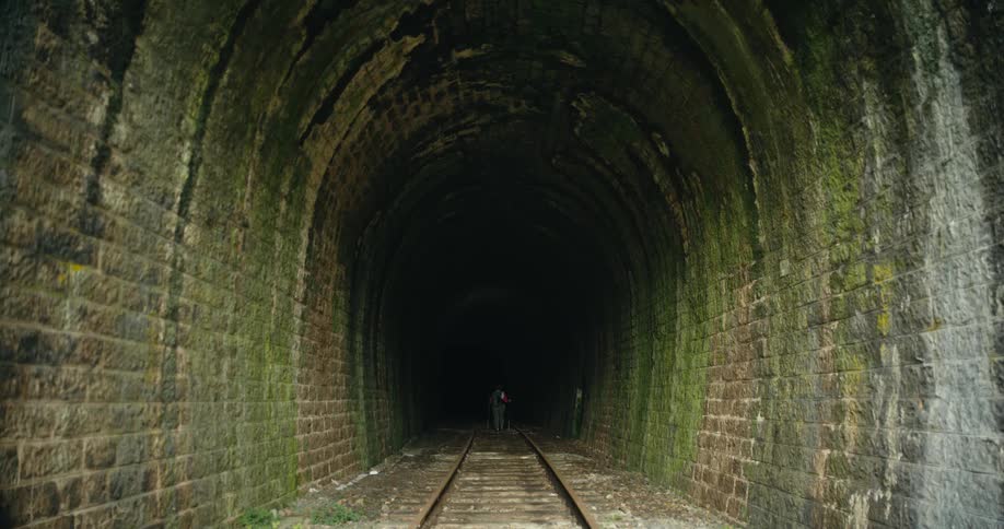 Hiker stands in moss covered brick walled train tunnel