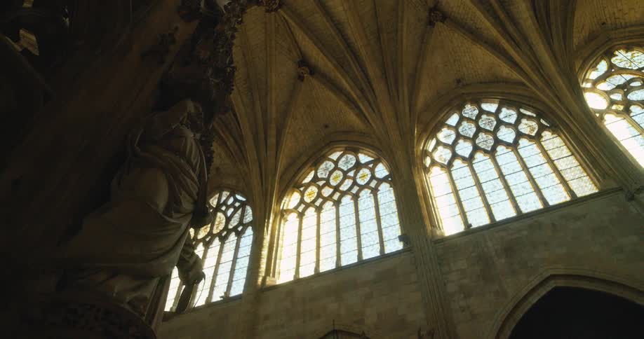 Stained glass window arches are high up near the ceiling of a church