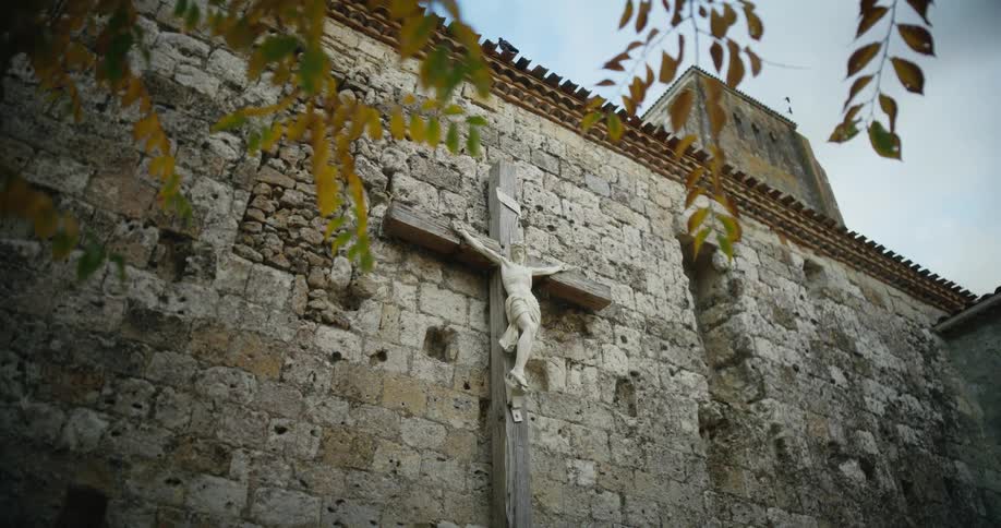 A statue of jesus christ on a wooden cross mounted on a stone wall outdoors during the day