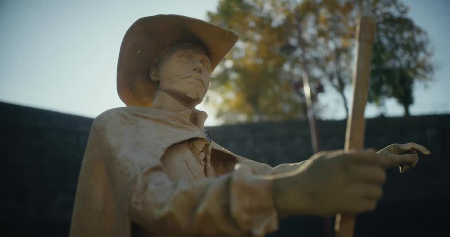 Sunlight shines over a stone structure onto a sculpture of a man