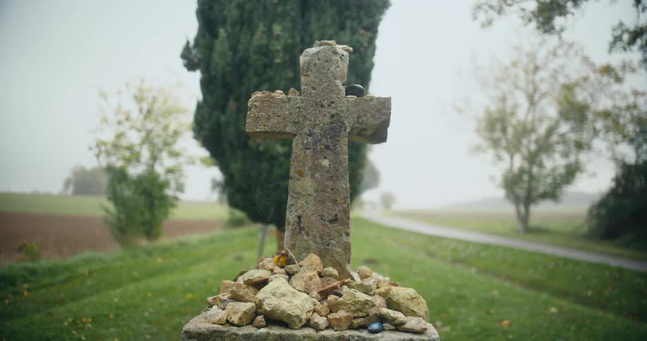 A cross and rocks are outside in the daytime surrounded by trees