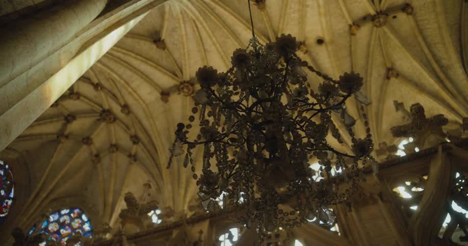 Sun shines through stained glass windows set high near vaulted ceiling of cathedral and onto elaborate chandelier