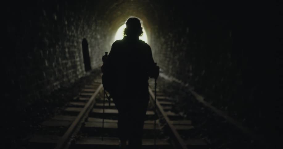 A hiker using trekking poles hikes along a railway through a tunnel during the day