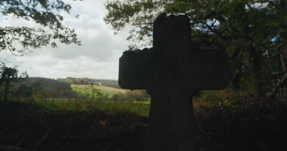 Close up of a stone cross on the ground under the shadows of the trees in the countryside