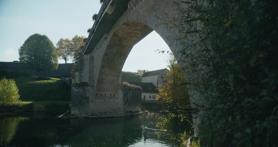 A stone bridge spanning a river in a rural area during the day