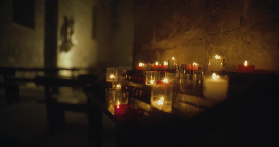 Rows of votive candles over a rack inside the dimly lit hallways of a church