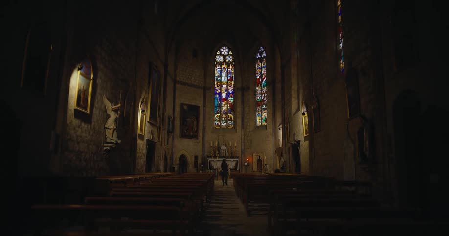 A weak person walks down the aisle of a dimly lit church in front of the altar