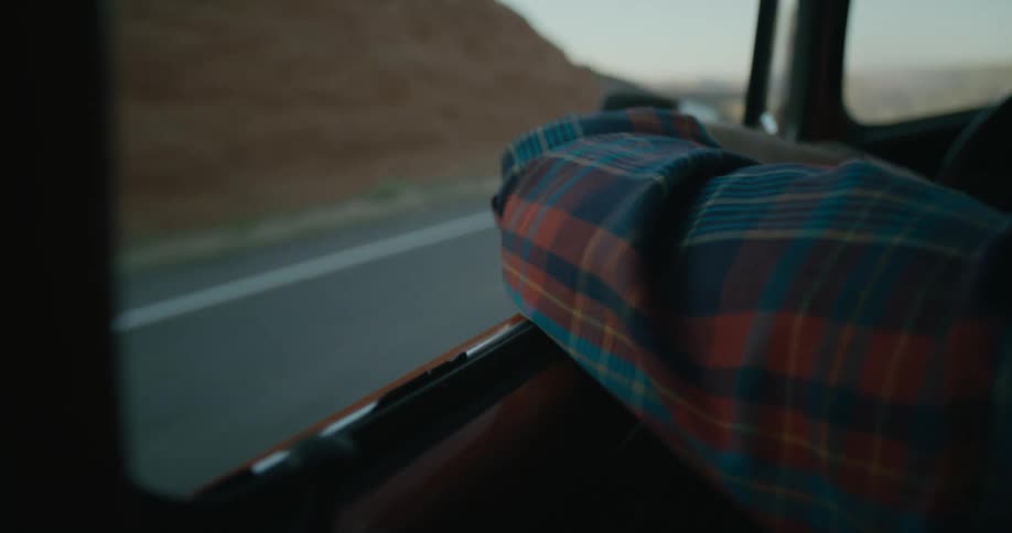 A person is resting their arm on the door while driving on a country highway