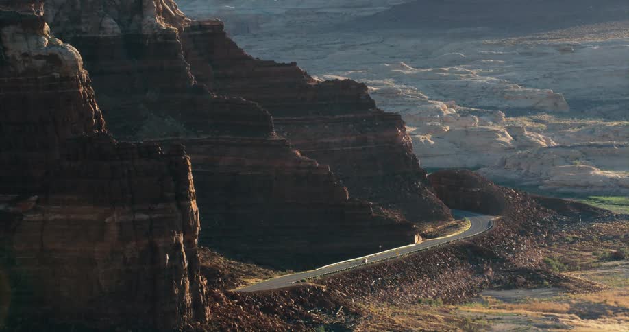Vehicle drives along highway curving along base of ridged mountain
