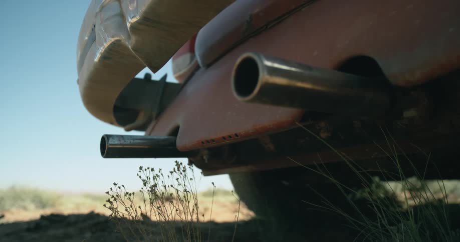 The tailpipes on a car are shaking and blowing weeds as the car starts