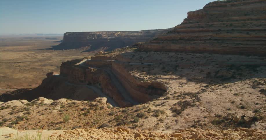 The sun shines on rock formations and mesa in the desert under a clear sky