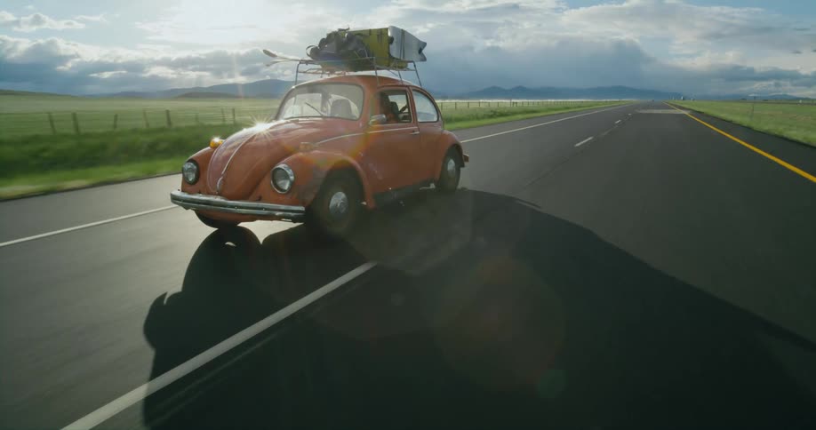 Orange classic volkswagen with luggage on the roof drives on a road through the countryside