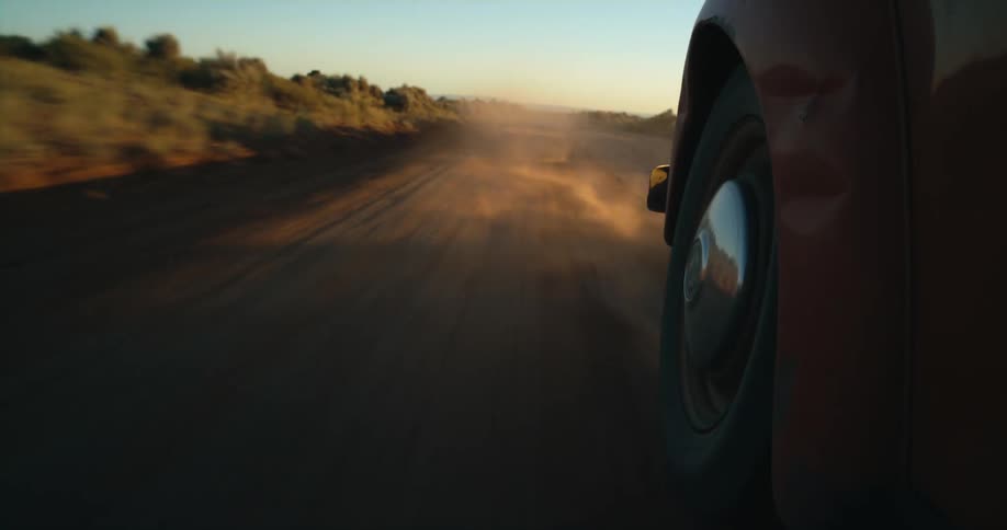 A volkswagen bug is speeding down a rural dirt road