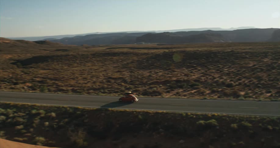 A vehicle travels along a road through a vast shrubland during the day