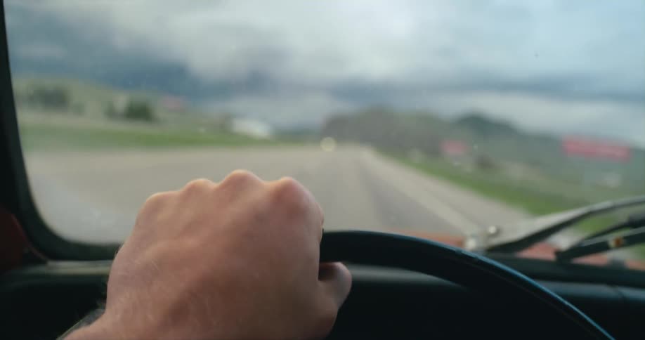 A man drives a vehicle along a road through the countryside during the day