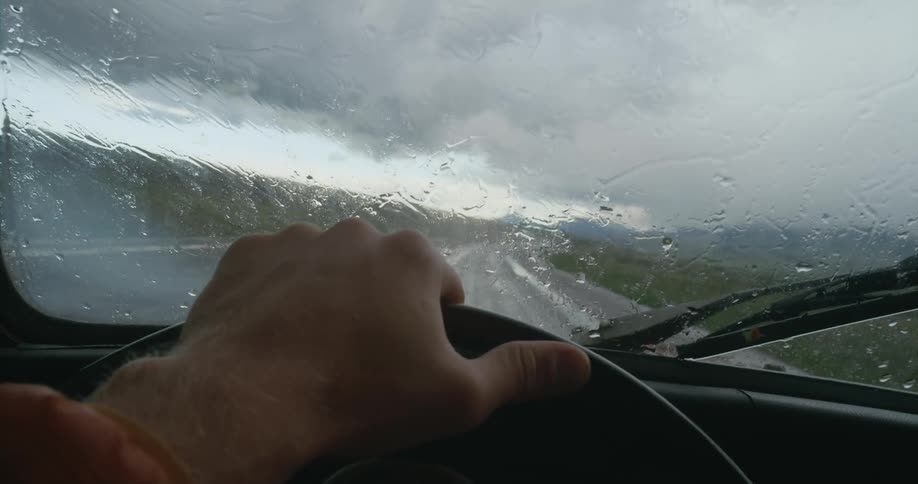 A person drives a vehicle along a road through the countryside on a rainy day