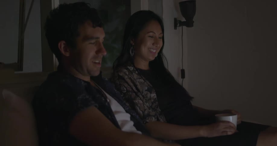 A man and woman sit on the couch watching something on a laptop