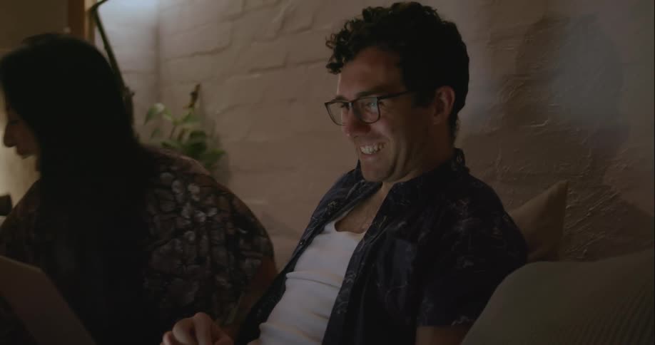 A man and woman laugh while looking at a laptop