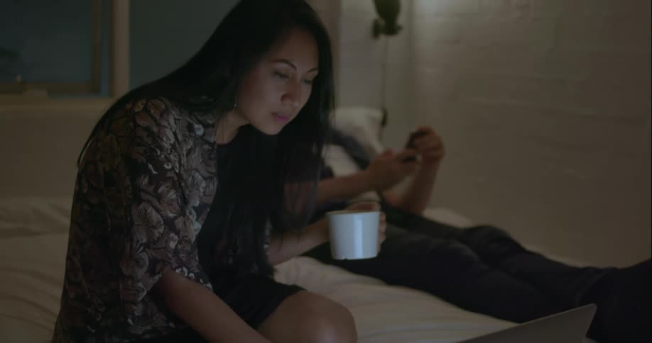 A woman is typing on her laptop in bed
