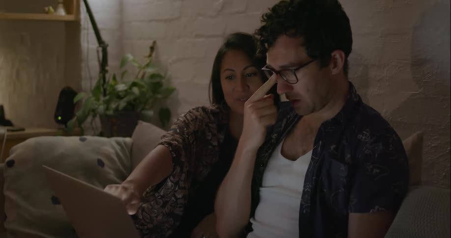A couple sit on the couch looking at a laptop and talking