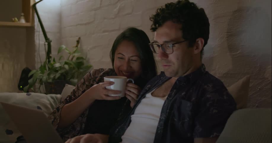 A woman laughs as she watches something on the laptop with a man