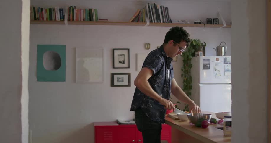 A man is using a knife to cut food at his kitchen counter