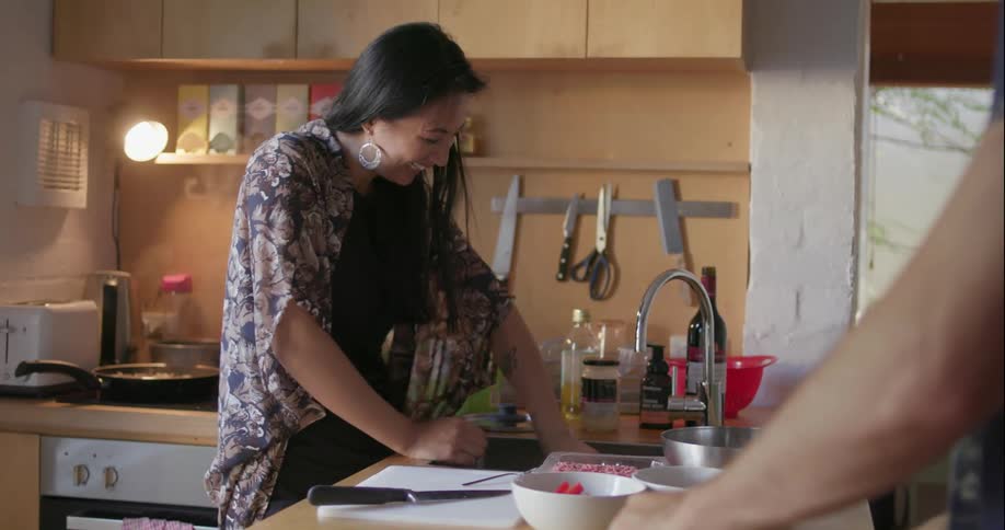 A woman laughs and washes up in a kitchen while cooking
