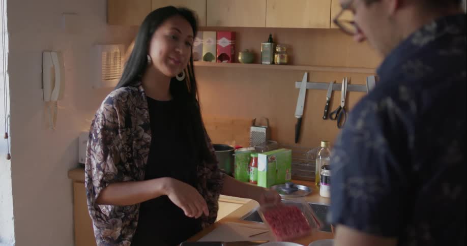 A woman is cooking and talking to a man at the table