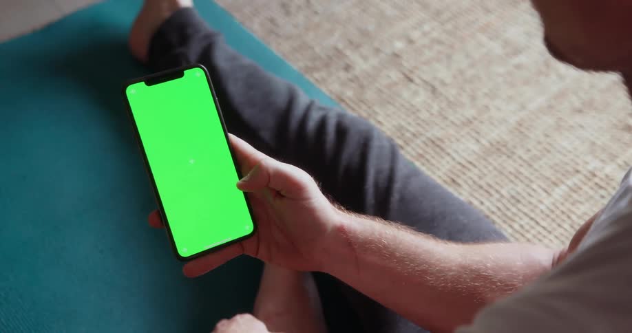 A man looks at a cell phone with a green screen