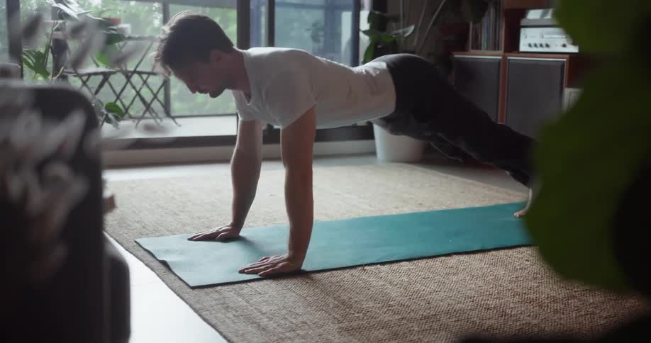 A man does push ups on a yoga mat in the living room