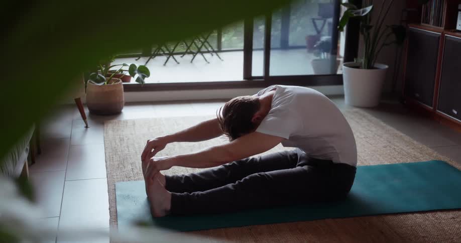 A man stretches on a yoga mat at home