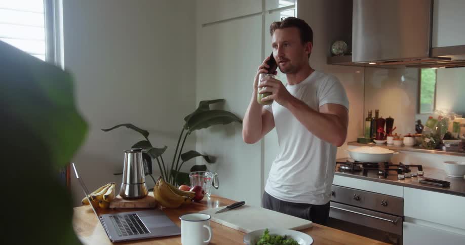 A man holds a green smoothie and talks on the phone