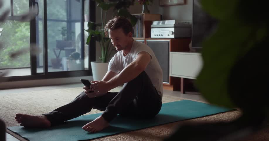Man sits on a yoga mat looking at a phone