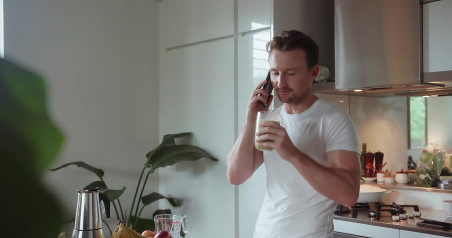 A man holds a green smoothie and talks on the phone