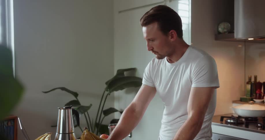 A man drinks a green smoothie and uses a laptop