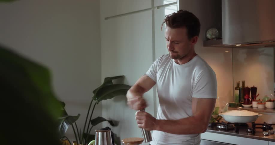 A man turns the handle of a grinder while standing in a kitchen